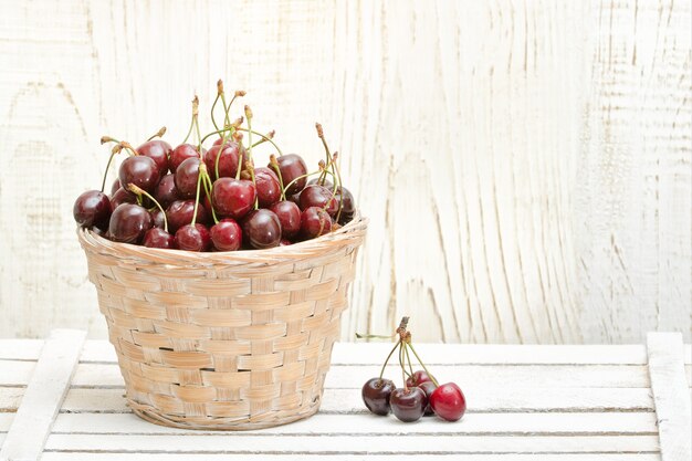 Cesta com cerejas em uma mesa de madeira branca