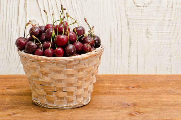 Cesta com cerejas em uma mesa de madeira, espaço vazio