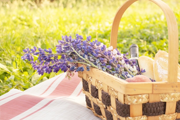 Cesta com flores vinho pêssegos e baguetes no fundo da grama de verão brilhante