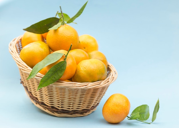 Cesta com tangerinas e uma por fora, todas colocadas sobre fundo azul