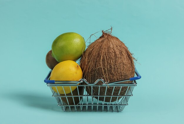 Cesta de la compra y frutas tropicales sobre fondo azul. Compras en el supermercado. Concepto de comida sana.
