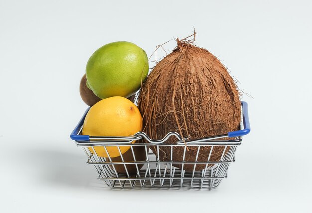 Cesta de la compra y frutas tropicales sobre fondo blanco. Compras en el supermercado. Concepto de comida sana.