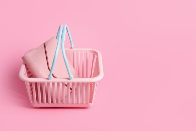 Cesta de la compra de plástico de colores con billetera de cuero. Cesta de supermercado vacía de color rosa y azul sobre fondo rosa pastel. Diseño creativo, compras, viernes negro, descuento, publicidad, concepto de venta.
