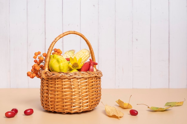 Cesta de cosecha de otoño con manzanas de maíz, calabacín y pimientos sobre un fondo de madera decorado con flores de otoño