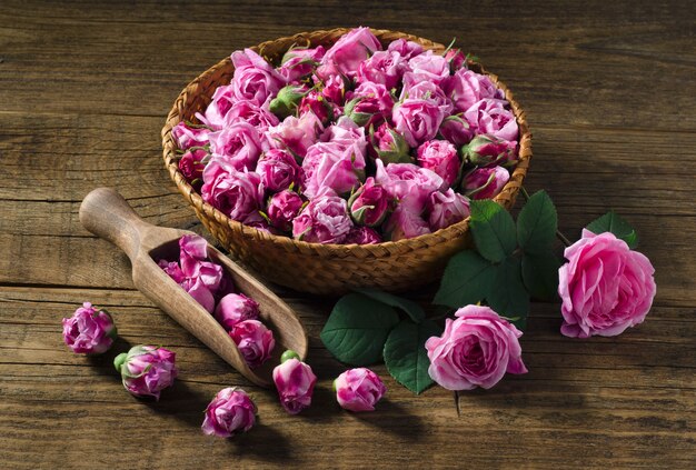 Cesta y cuchara de madera con té fresco capullos de rosa sobre mesa de madera. Ã Â¡lose-up. Estilo rústico.