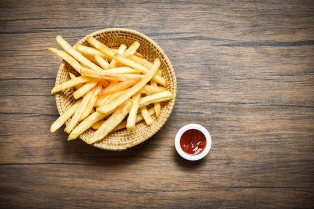 Cesta de batatas fritas e ketchup no fundo da mesa de jantar de madeira