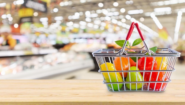 Cesta de compras com frutas na mesa de madeira sobre o fundo do desfoque do supermercado da mercearia