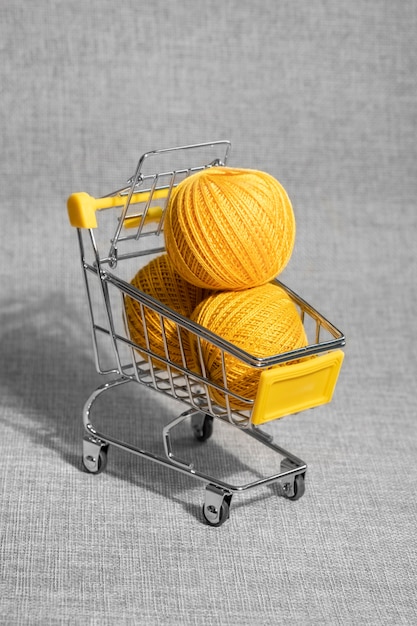 Cesta de compras sobre rodas. Bolas de fios amarelos para tricô.