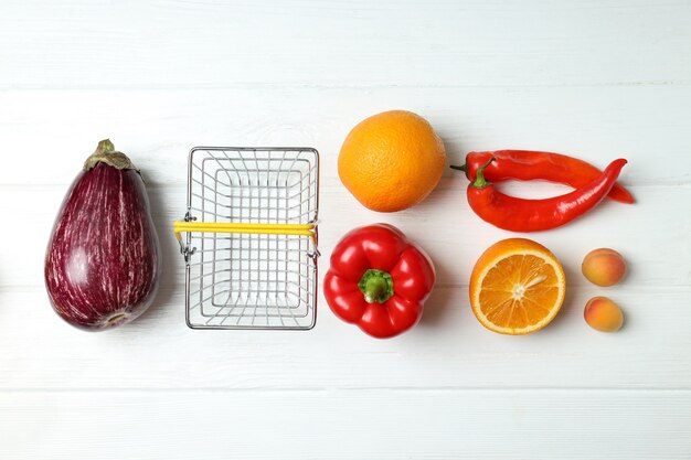 Cesta de compras, vegetais e frutas na mesa de madeira branca