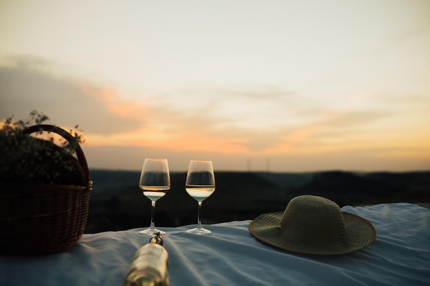 Cesta de copos de vinho de garrafa de vinho branco com flores brancas e chapéu de palha no piquenique de verão