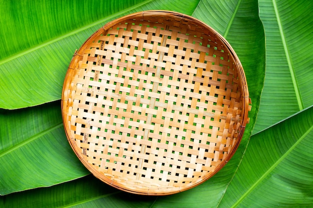 Cesta de debulha de bambu de madeira vazia em fundo de folhas de bananeira. vista do topo