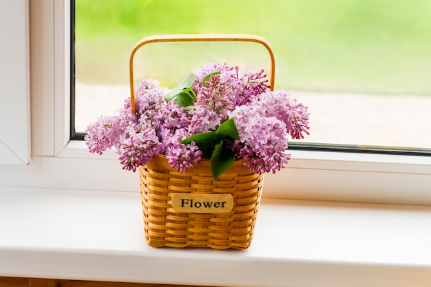 Cesta de flores decorativas com ramos de lilases primavera no parapeito da janela de uma casa de campo. o conceito de um bom humor de primavera.