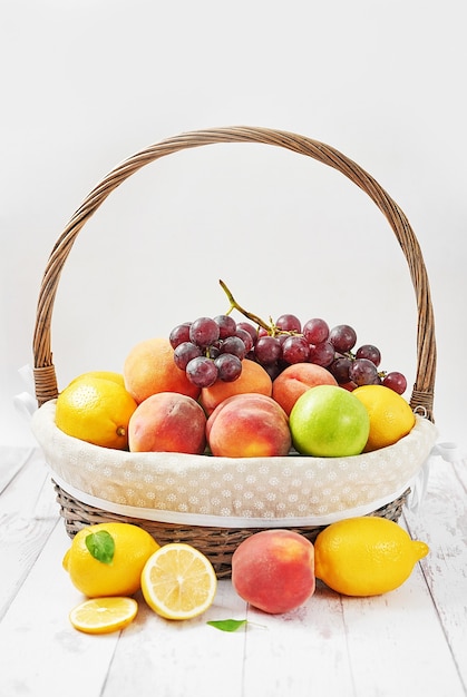 Foto cesta de frutas maçãs, pêssegos, limões, uvas