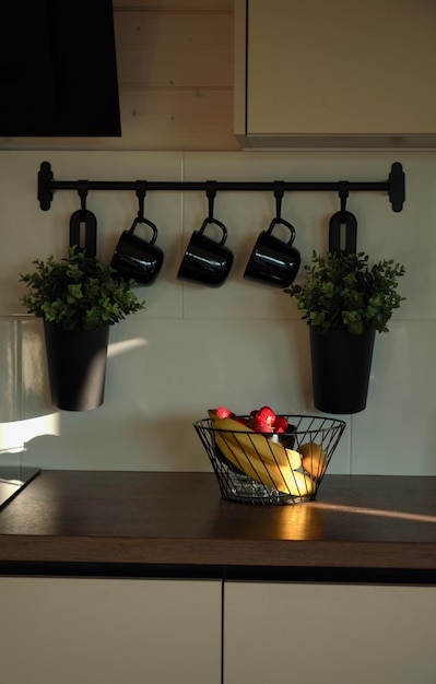Foto cesta de frutas na bancada da cozinha com canecas penduradas na parede