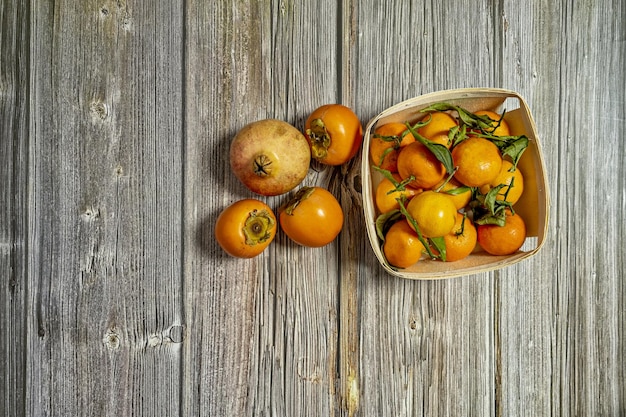 Cesta de madeira com um quilo de tangerinas maduras com algumas folhas verdes alguns caquis e uma romã