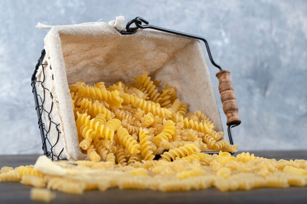 Foto cesta de massa fusilli seca crua na mesa escura.