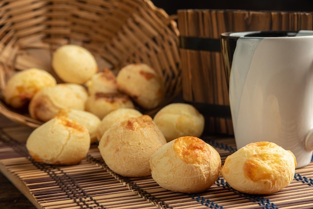 Cesta de pão de queijo com pão de queijo deitado sobre uma esteira de tecido de madeira e acessórios foco seletivo de fundo escuro