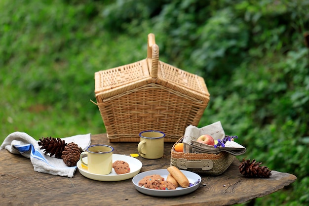 Cesta de piquenique com frutas e padaria na velha mesa de madeira rústica com paisagem verde