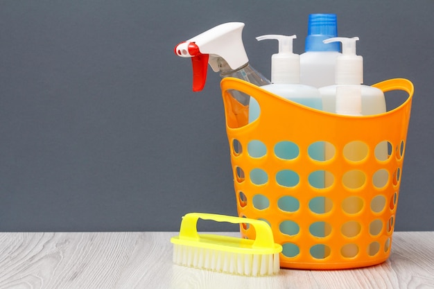 Cesta de plástico com frascos de detergente, limpador de vidros e azulejos, detergente para micro-ondas e fogões com escova em fundo cinza. Conceito de lavagem e limpeza.