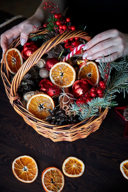 Cesta de vime com bastões de rebuçados às riscas, laranjas fatiadas e secas, cones e presentes.