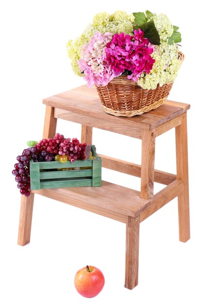 Cesta de vime com flores e frutas em caixa de madeira em pequena escada de madeira isolada em branco