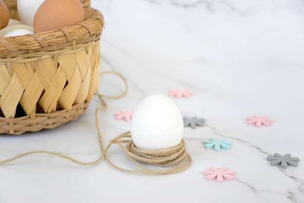 Cesta de vime com ovos e um único ovo branco na corda com flores coloridas sobre fundo de mármore. feliz páscoa.