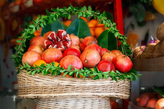 Cesta decorada con hojas verdes frescas con jugosas frutas granadas maduras y naranjas preparadas para exprimir jugo en un café de la calle.