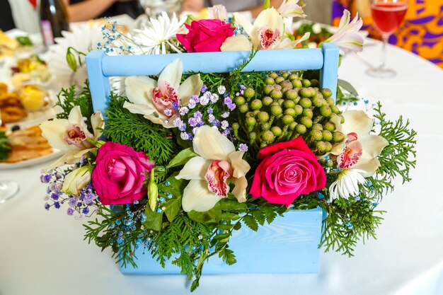 Cesta con flores en un juego sobre una mesa de banquete con un mantel blanco. Foto horizontal