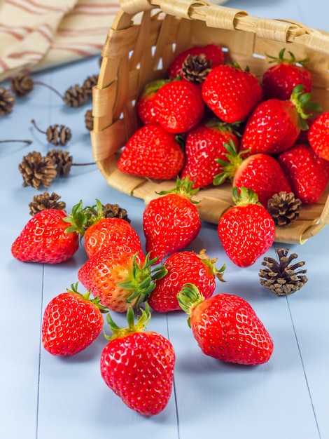 Cesta con fresas y conos de abeto derramándose sobre una mesa