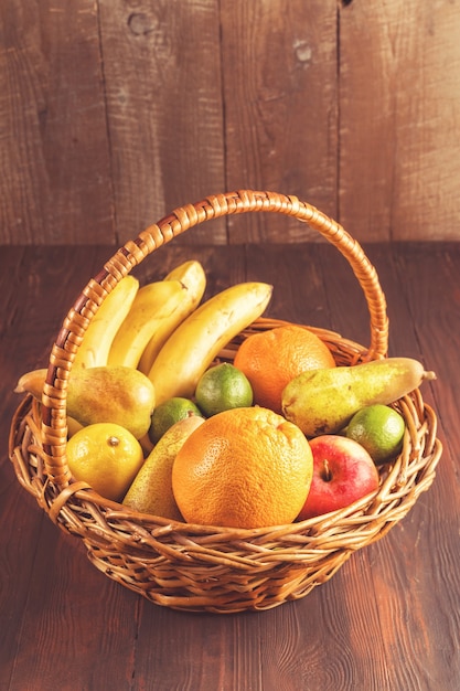 Foto cesta y frutas frescas en la mesa de madera y fondo de madera, imagen de tonos.