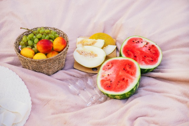 Una cesta de frutas, uvas, melocotones, melón, sandía, yacen sobre una manta, sombrero de paja y gafas, picnic en la naturaleza