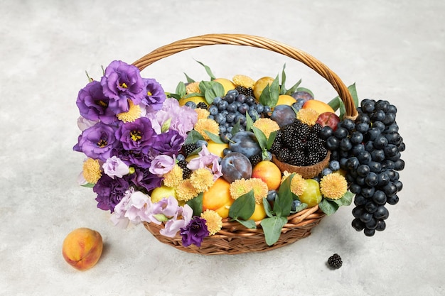 Cesta grande com frutas maduras e flores roxas em um fundo cinza