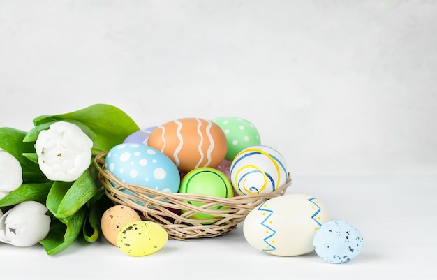 Cesta con huevos de Pascua y un ramo de tulipanes blancos sobre un fondo gris claro