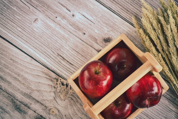 Foto cesta de madera con manzanas rojas frescas y montón de espigas de granos de trigo maduro en la superficie de la tabla de madera vieja. vista superior composición plana laico. espacio para plantilla de texto