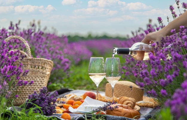 Cesta de mimbre con comida deliciosa para un picnic romántico en un campo de lavanda La niña vierte vino