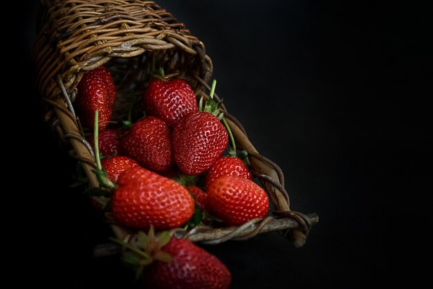 Cesta de mimbre descansa sobre una superficie oscura llena de rojo srtawberries maduras fondo de alimentos de verano