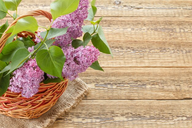 Cesta de mimbre con flores lilas sobre tablas de madera. Vista superior con espacio de copia.