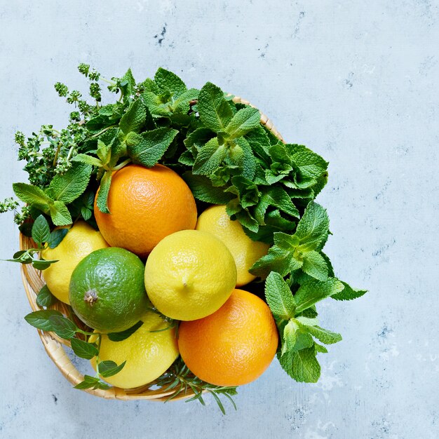 Cesta de mimbre con limones, limas, naranjas y menta fresca sobre un fondo azul. Conjunto de cítricos de frutas para hacer limonada fresca de verano.