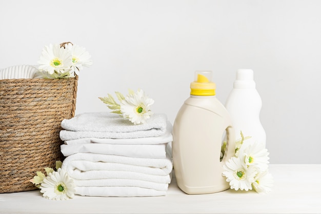 Cesta de mimbre con lino blanco, gel de lavado y suavizante sobre una mesa blanca con flores de gerbera. Maqueta día de lavandería de primavera.