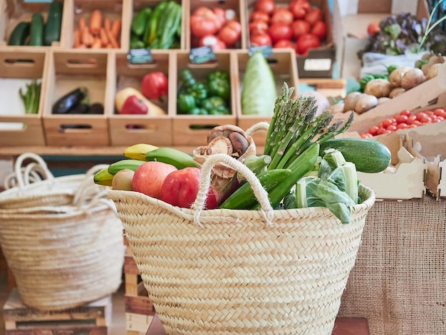 Cesta de mimbre llena de verduras y frutas en una pequeña tienda local de alimentos orgánicos En los estantes de fondo con otros productos en cajas de madera Concepto de estilo de vida saludable y sostenible