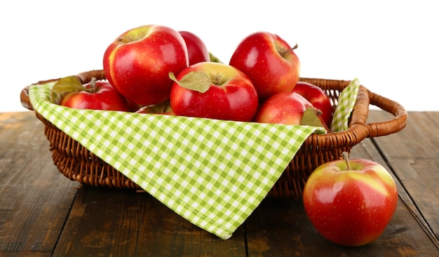 Cesta de mimbre de manzanas rojas con servilleta sobre mesa de madera aislado sobre fondo blanco.