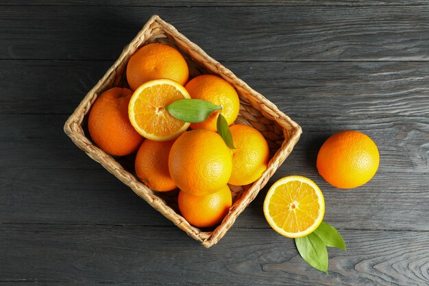 Cesta de mimbre con naranjas maduras en mesa de madera.