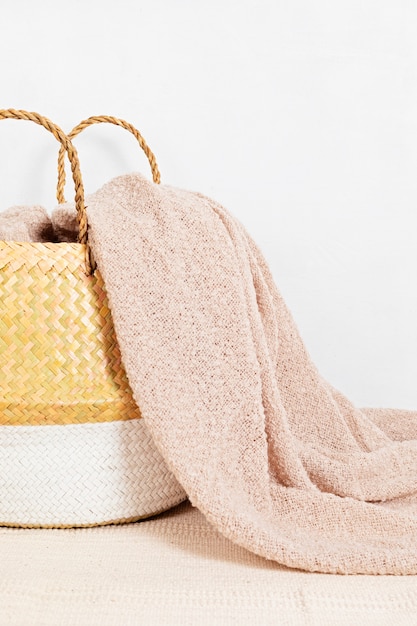 Cesta de mimbre de paja con manta suave beige, primer plano. Elegante artículo de decoración del hogar higge ecológico