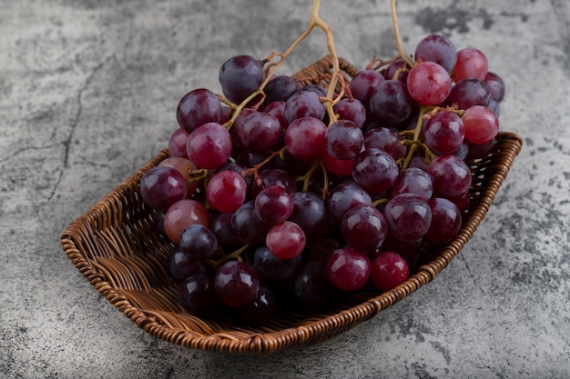 Cesta de mimbre de uvas rojas frescas sobre fondo de piedra.