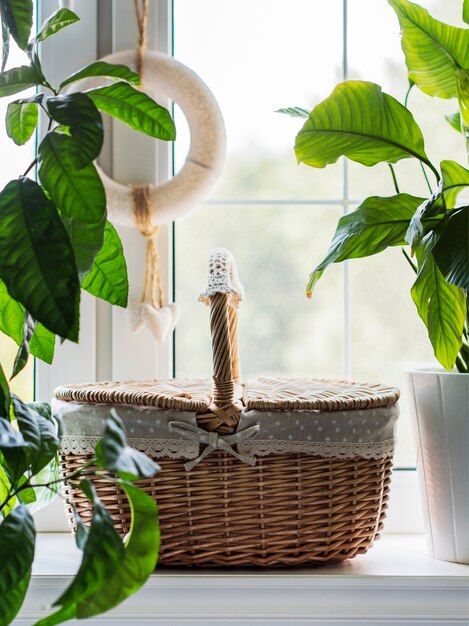 Cesta de mimbre vintage en el alféizar de la ventana con plantas verdes