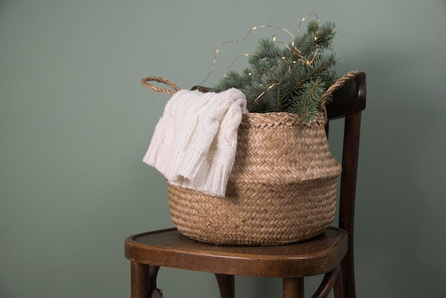 Cesta de paja rústica de decoración navideña con ramas de abeto en una silla de fondo verde