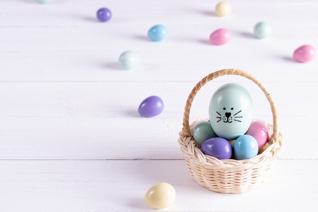 La cesta de Pascua llenó de los huevos coloridos en el fondo de madera blanco. Copia espacio