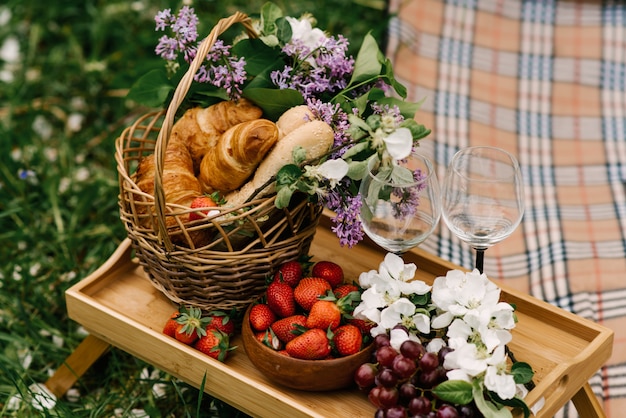 Cesta de picnic con fresas, uvas y bollos sobre la hierba verde en el jardín