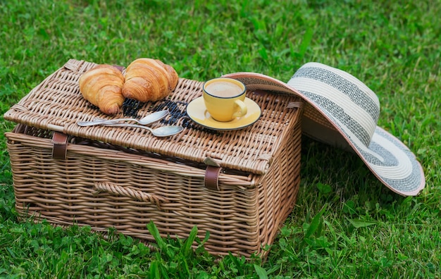 Cesta de picnic de mimbre sobre la hierba verde con comida y café.