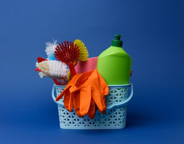 Foto cesta de plástico azul con cepillos, esponjas y guantes de goma para limpiar, fondo azul.